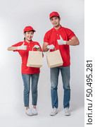 Image of a happy young delivery man in red cap blank t-shirt uniform standing with empty brown craft paper packet isolated on light gray background studio. Стоковое фото, агентство Ingram Publishing / Фотобанк Лори
