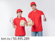 Image of a happy young delivery man in red cap blank t-shirt uniform face mask gloves standing with empty brown craft paper packet isolated on light gray background studio, Service during pandemic coronavirus virus covid-19 concept. Стоковое фото, агентство Ingram Publishing / Фотобанк Лори