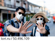 selective focus hands of young backpacker couple in protection face mask and sunglasses keep distance raise palms express negative attitude coronavirus don’t close contact while travel in city street. Стоковое фото, агентство Ingram Publishing / Фотобанк Лори
