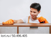 Asian young handsome man was spray disinfectant bottle and using cloth wipes on the wooden cabinet with drawer to cleaning furniture at home. Стоковое фото, агентство Ingram Publishing / Фотобанк Лори