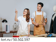 Portrait Young handsome man and pretty woman in glasses wearing apron, Couple fashion designer working together with happy, mannequin and tailoring tools on desk at studio. Стоковое фото, агентство Ingram Publishing / Фотобанк Лори