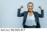 Portrait of Asian woman keeps hands clenched in fists with positiveness as achieved success in career, smiling, showing strong powerful, isolated over background with copy space. Стоковое фото, агентство Ingram Publishing / Фотобанк Лори