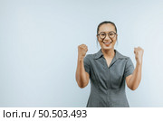 Portrait of Asian woman glasses keeps hands clenched in fists with positiveness as achieved success in career, smiling, showing strong powerful, isolated over background with copyspace. Стоковое фото, агентство Ingram Publishing / Фотобанк Лори