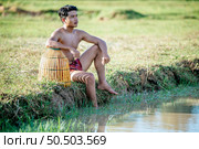 Portrait Young man topless use bamboo fishing trap to catch fish for cooking, Asian young farmer man in rural lifestyle, blurred buffalo is soaking in the swamp. in background. Стоковое фото, агентство Ingram Publishing / Фотобанк Лори