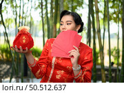 Portrait pretty Asian woman in a Chinese cheongsam posing envelopes fan with Red amulet bag with Chinese alphabet means good fortune and happinese in bamboo forest background, Chinese New Year concept. Стоковое фото, агентство Ingram Publishing / Фотобанк Лори