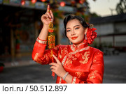 Portrait Asian beautiful woman wearing a cheongsam smiling and holding china auspicious amulet pose at shrine on Chinese New Year, copy space. Стоковое фото, агентство Ingram Publishing / Фотобанк Лори