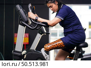 Young female with one prosthetic leg with exercising with a spinning bike in the gym to practice joint use with the other normal leg to be flexible, Concept of living a woman’s life with a prosthetic. Стоковое фото, агентство Ingram Publishing / Фотобанк Лори