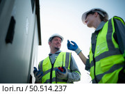 A team of electrical engineers is inspecting an energy storage station of a solar panels in the middle of a hundred acre field of solar panels. Стоковое фото, агентство Ingram Publishing / Фотобанк Лори