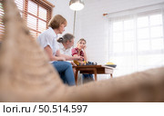 In the living room of the house, an elderly couple sits and relaxes. to begin playing chess together with a chess board with a daughter cheering beside him. Стоковое фото, агентство Ingram Publishing / Фотобанк Лори