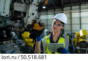 A female engineer installs a program on a robotics arm in a robot warehouse. And test the operation before sending the machine to the customer. Стоковое фото, агентство Ingram Publishing / Фотобанк Лори