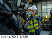 A female engineer installs a program on a robotics arm in a robot warehouse. And test the operation before sending the machine to the customer. Стоковое фото, агентство Ingram Publishing / Фотобанк Лори