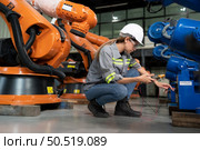 In the robots warehouse, A female engineer inspects the electrical system of every robotics arm, before delivering to the customer. Стоковое фото, агентство Ingram Publishing / Фотобанк Лори