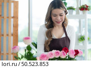 ?Young woman florist smelling a red rose in the flower shop. Стоковое фото, агентство Ingram Publishing / Фотобанк Лори