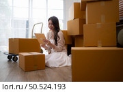 Young asian woman checking boxes being transported into new home with tablet. Стоковое фото, агентство Ingram Publishing / Фотобанк Лори