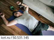 Funny overweight man in glasses closed his eyes and lying exhausted down on the floor after workout, copy space. Стоковое фото, агентство Ingram Publishing / Фотобанк Лори