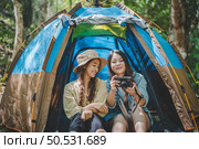  Young pretty taking photo by camera and showing picture to her friend while sitting at the camping tent in forest, Young Asian group women travel outdoor camping. Стоковое фото, агентство Ingram Publishing / Фотобанк Лори