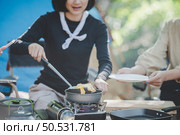 Young pretty girl put an egg on pan  while camping with her friends, cooking easy meal in nature park, They are enjoy to discussion and laugh with fun together, copy space. Стоковое фото, агентство Ingram Publishing / Фотобанк Лори