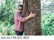 Portrait of Happy Asian man hugging a tree in forest. Protecting and love nature. Environment and ecology concept. Стоковое фото, агентство Ingram Publishing / Фотобанк Лори
