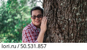 Portrait of Happy Asian man hugging a tree in forest. Protecting and love nature. Environment and ecology concept. Стоковое фото, агентство Ingram Publishing / Фотобанк Лори