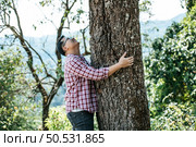 Portrait of Happy Asian man hugging a tree in forest. Protecting and love nature. Environment and ecology concept. Стоковое фото, агентство Ingram Publishing / Фотобанк Лори