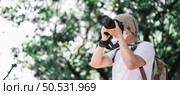 Asian traveler man with backpack taking a photo in the park with copy space. Travel photographer. Vocation and holiday concept. Стоковое фото, агентство Ingram Publishing / Фотобанк Лори