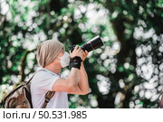 Asian traveler man with backpack taking a photo in the park with copy space. Travel photographer. Vocation and holiday concept. Стоковое фото, агентство Ingram Publishing / Фотобанк Лори
