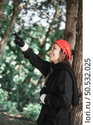 Portrait of Happy Asian young woman in winter costume pointing aside at the forest. Vacation and travel concept. Стоковое фото, агентство Ingram Publishing / Фотобанк Лори