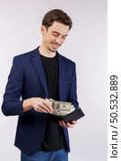Excited young man putting banknotes into wallet isolated white studio background. Finance, investment and money saving concept. Стоковое фото, агентство Ingram Publishing / Фотобанк Лори