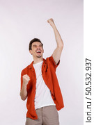 Portrait of happy joyful young man standing doing winner gesture clenching fists keeping isolated on white color wall background studio. Victory and success concept. Стоковое фото, агентство Ingram Publishing / Фотобанк Лори