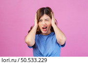 Portrait of angry irritated young woman wearing casual t-shirt covering her ears with hands and shouting while standing isolated over pink background. Expression, people and lifestyle concept. Стоковое фото, агентство Ingram Publishing / Фотобанк Лори