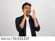 Portrait of Young asian man in blue shirt shout story or making announcement isolated on white background. Advertising and lifestyle concept. Стоковое фото, агентство Ingram Publishing / Фотобанк Лори