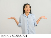 Portrait of confused young asian woman in blue shirt shrugging shoulders in bewilderment isolated on white background. Expression and lifestyle concept. Стоковое фото, агентство Ingram Publishing / Фотобанк Лори
