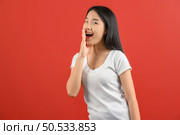 Portrait of Young asian woman in white t-shirt shout story or making announcement isolated on red background. Advertising and lifestyle concept. Стоковое фото, агентство Ingram Publishing / Фотобанк Лори