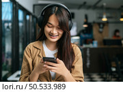 Pretty asian woman sitting and enjoy to listening musice from wireless headphone and singing together with smartphone at cafe, relaxing and lifestyle concept. Стоковое фото, агентство Ingram Publishing / Фотобанк Лори