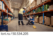 A warehouse worker consoles and helps a female worker who cries out in pain after a leg accident in a large warehouse. Стоковое фото, агентство Ingram Publishing / Фотобанк Лори