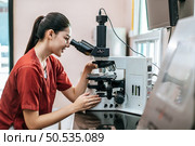 Asian young female farmer looking through a microscope in a laboratory. Modern technologies in agriculture management, agribusiness and research concept. Стоковое фото, агентство Ingram Publishing / Фотобанк Лори