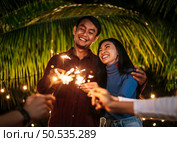 Portrait of Happy Asian group of friends having fun with sparklers outdoor - Young people having fun with fireworks at night time  - People, food, drink lifestyle, new year celebration concept. Стоковое фото, агентство Ingram Publishing / Фотобанк Лори