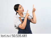 Portrait Asian young woman smile with happy in waitress uniform and apron, Cheerful girl standing with hand signal, point finger isolated on white background. Стоковое фото, агентство Ingram Publishing / Фотобанк Лори