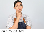 Portrait of young asian woman in waitress costume standing and thinking, free space to put products for advertisement isolated on white background. Стоковое фото, агентство Ingram Publishing / Фотобанк Лори