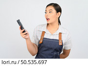 Portrait of young asian woman in waitress uniform use smartphone with feel surprise, copy space for insert products for advertisement isolated on white background. Стоковое фото, агентство Ingram Publishing / Фотобанк Лори