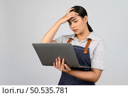 Portrait of young asian woman in waitress uniform looking on laptop computer monitor with feel stress posture, copy space to insert products for advertisement isolated on white background. Стоковое фото, агентство Ingram Publishing / Фотобанк Лори
