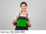 Portrait of young asian woman in waitress uniform use digital pen point on mock up tablet posture, copy space on green screen to insert products for advertisement isolated on white background. Стоковое фото, агентство Ingram Publishing / Фотобанк Лори