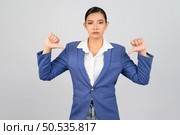 Portrait Asian young woman in officer uniform standing showing thumb down posture, Pretty girl grimace with dissatisfaction and make hand thumb down gestures, isolated on white background. Стоковое фото, агентство Ingram Publishing / Фотобанк Лори