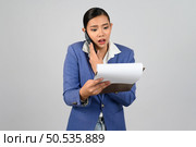 Portrait Asian young woman in officer uniform standing talking with mobile phone during read report paper on clipboard in hand with feel shock posture,  isolated on white background. Стоковое фото, агентство Ingram Publishing / Фотобанк Лори