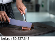 Young chef cutting medium-rare steak after it has been done grilling. Стоковое фото, агентство Ingram Publishing / Фотобанк Лори