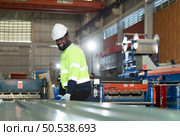 Young engineers engineers testing and confirming that the machinery at the factory that creates metal sheet tiles is functioning as intended. Стоковое фото, агентство Ingram Publishing / Фотобанк Лори