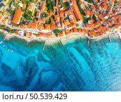 Aerial view of buildings with orange roofs, beach, clear blue sea in summer day. Vacation in beautiful Baska city, Krk island, Croatia. Top drone view of houses, streets, promenade, adriatic sea bay. Стоковое фото, агентство Ingram Publishing / Фотобанк Лори