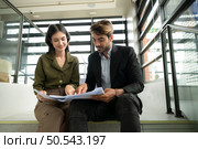 Both of businessperson sitting on stairs in office talk and exchange ideas on using natural energy in buildings before entering the meeting to present and consider. Стоковое фото, агентство Ingram Publishing / Фотобанк Лори