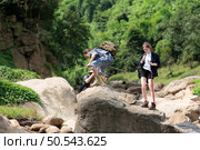 Young man hiker with backpack and trekking poles with a young man helping to pull him up to stand on the rock. Стоковое фото, агентство Ingram Publishing / Фотобанк Лори