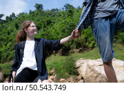 Young woman hiker with backpack and trekking poles with a young man helping to pull him up to stand on the rock. Стоковое фото, агентство Ingram Publishing / Фотобанк Лори